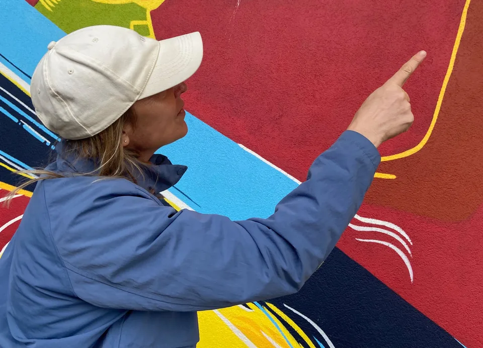 A player in a cap points out a clue on a bright Granville Island mural